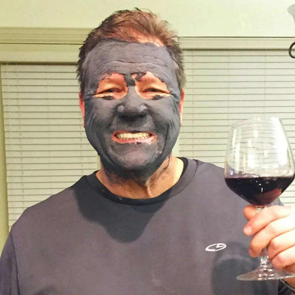 Man wearing organic activated charcoal face mask holding a glass of red wine