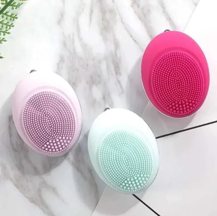 Compact ultrasonic plastic device face wash brushes in pink, white, and red colors on marble surface