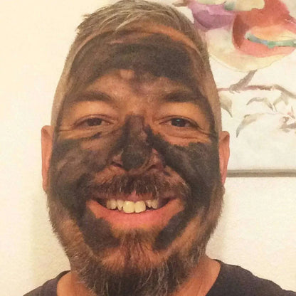 smiling man with organic activated charcoal face mask applied for detox and purification