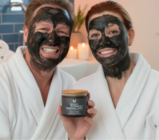 Smiling couple wearing organic activated charcoal face mask holding jar in spa setting