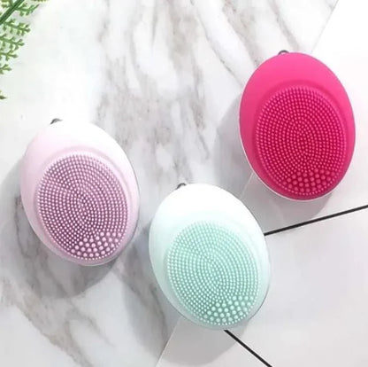 Compact ultrasonic plastic device face wash brushes in pink, white, and red colors on marble surface